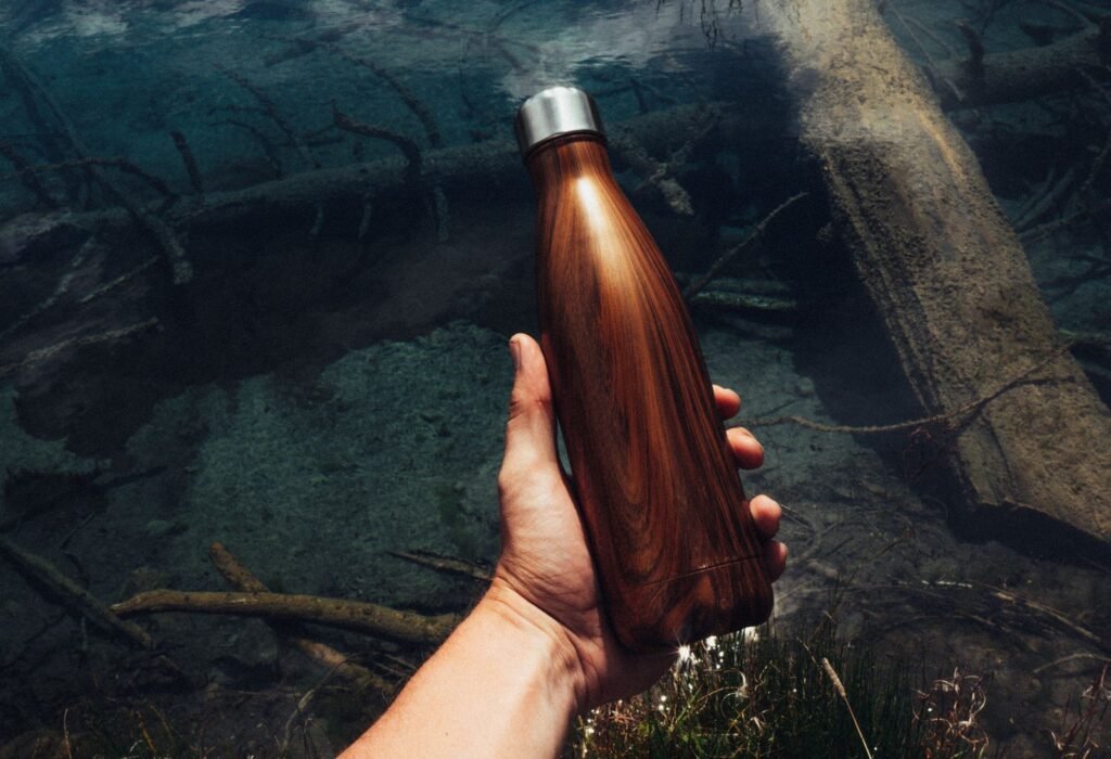 A hand holding a wood-grain stainless steel bottle over a clear stream